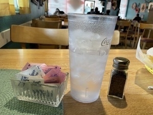 Photo of gigantic glass of water next to a pepper shaker and sweetener dish to show scale. The water cup towers over the two other objects. Taken at Francisca's Mexican Restaurant in Farmington New Mesico.