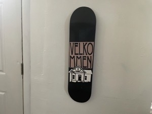 Photo of skateboard deck with design of house and the text 